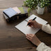 Person writing in an Apica CD Twin Ring Notebook on a desk with fountain pen friendly paper