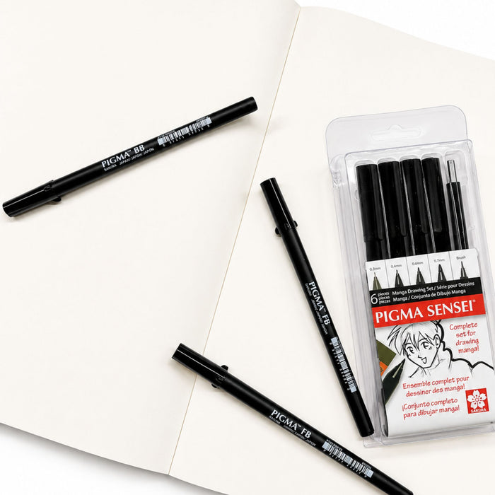 Open comic manga sketch pad with Pigma Sensei drawing pens on white paper
