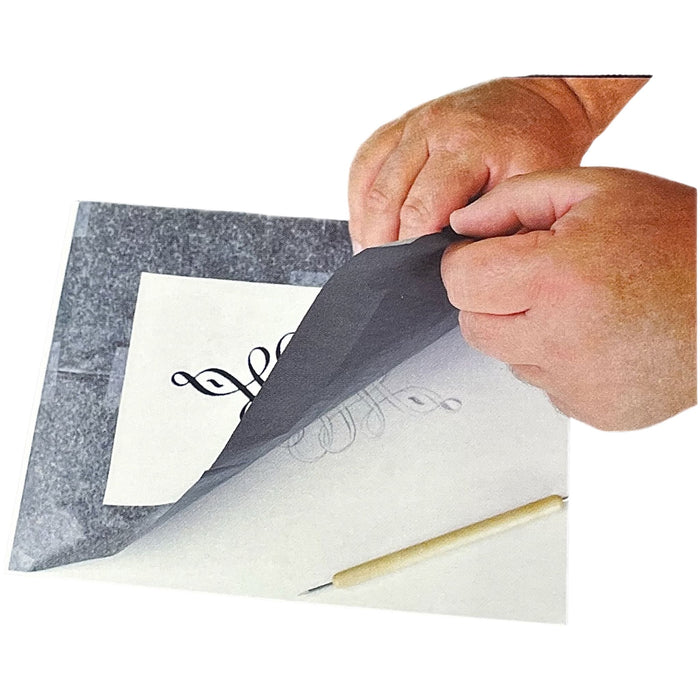 Artist lifting graphite transfer paper to reveal transferred design