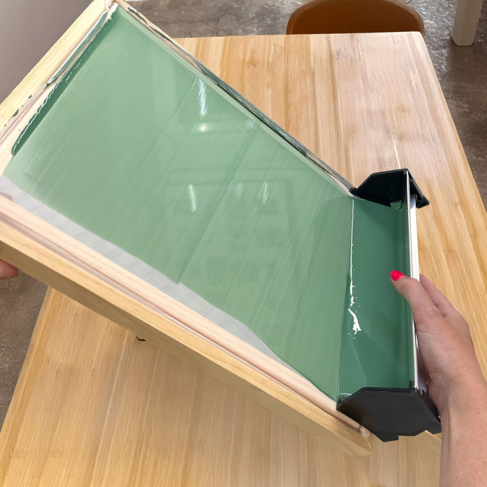Scoop coater being used to coat a wooden screen printing frame with photo emulsion