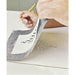 Artist lifting graphite transfer paper to reveal transferred design
