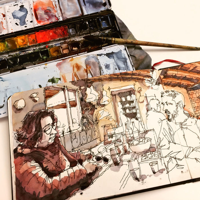 Watercolour sketchbook in use with paint palette, brush, and urban sketch illustration