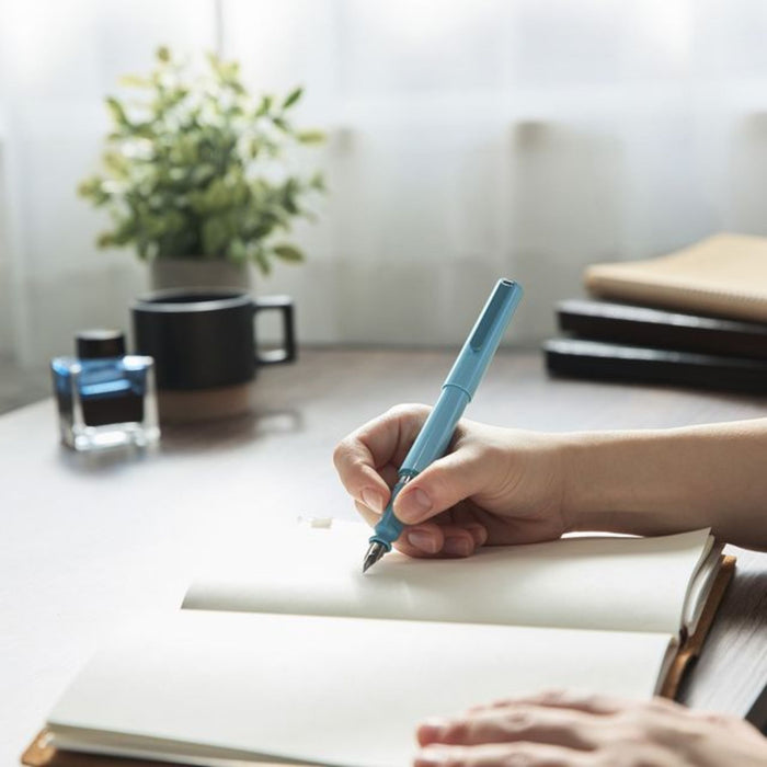 green fountain pen writing in notebook on desk with ink bottle and plant