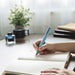 green fountain pen writing in notebook on desk with ink bottle and plant