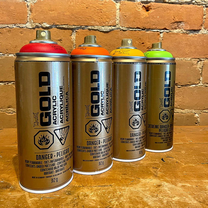 Four cans of Montana Gold spray paint in front of brick wall.